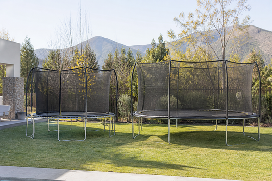 Comparación visual de camas elásticas grandes de 12 y 14 pies en un patio amplio