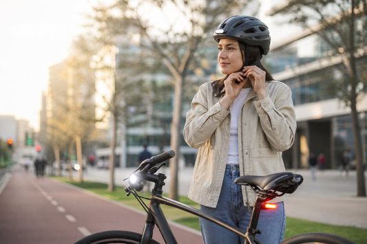 Persona ajustando un casco urbano junto a una bicicleta con luces LED en una ciclovía