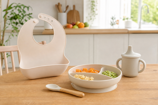 Set de alimentación bebé de silicona con plato, babero, cuchara y vaso sobre una mesa