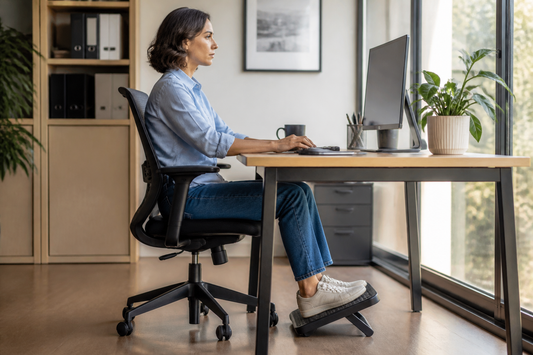 Persona trabajando sentada con los pies apoyados sobre un apoya pies bajo el escritorio